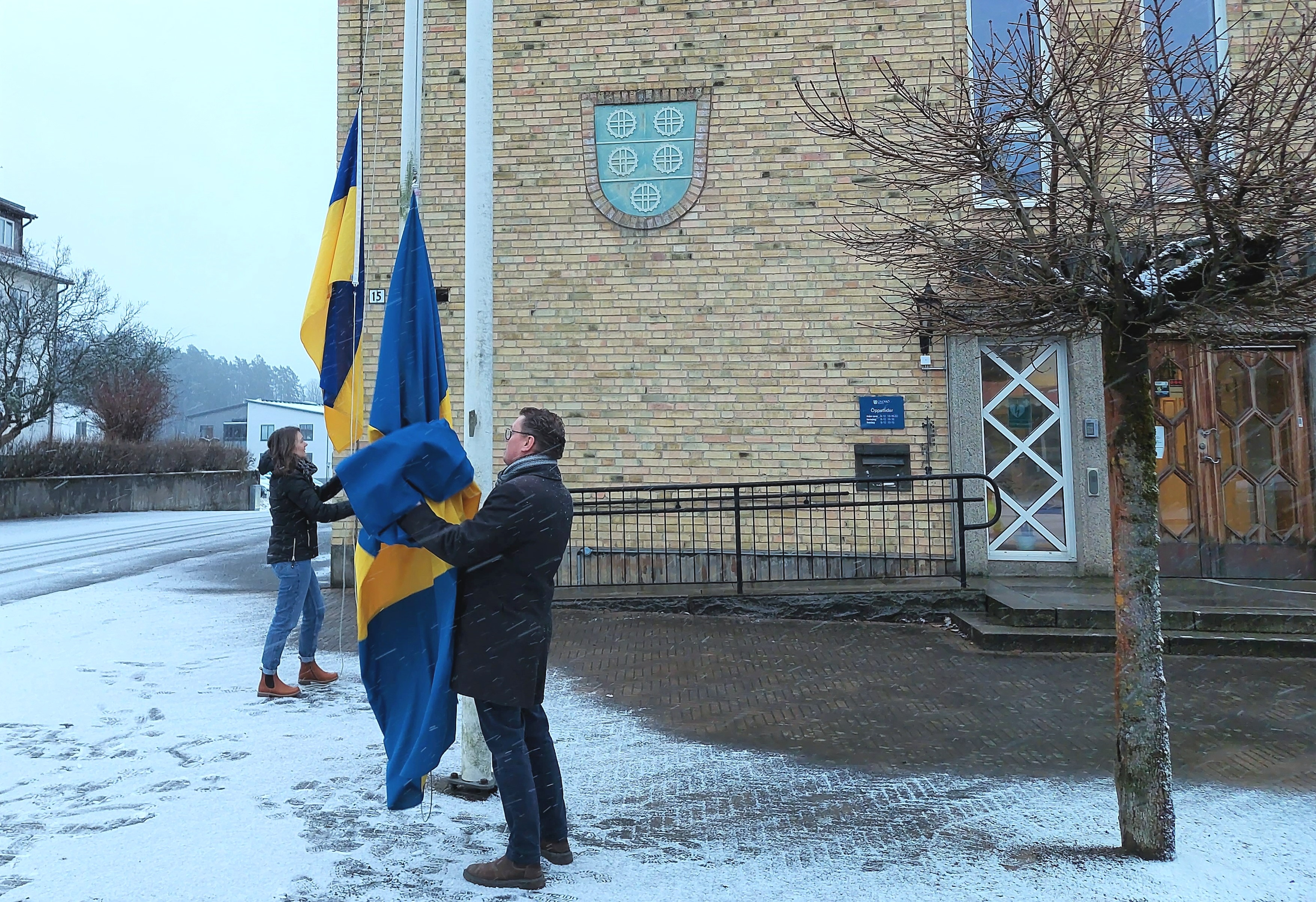 En kvinna hissar Ukrainas flagga och en man hissar svenska flaggan framför kommunhuset i Gnosjö.
