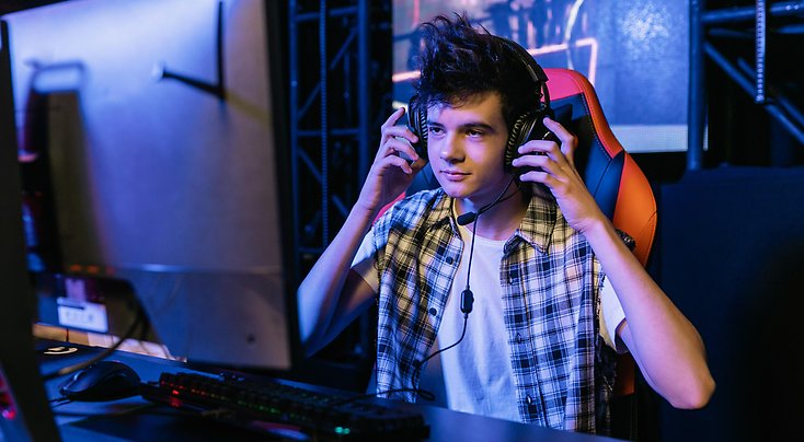 En pojke sitter framför en dator och har hörlurar på sig.