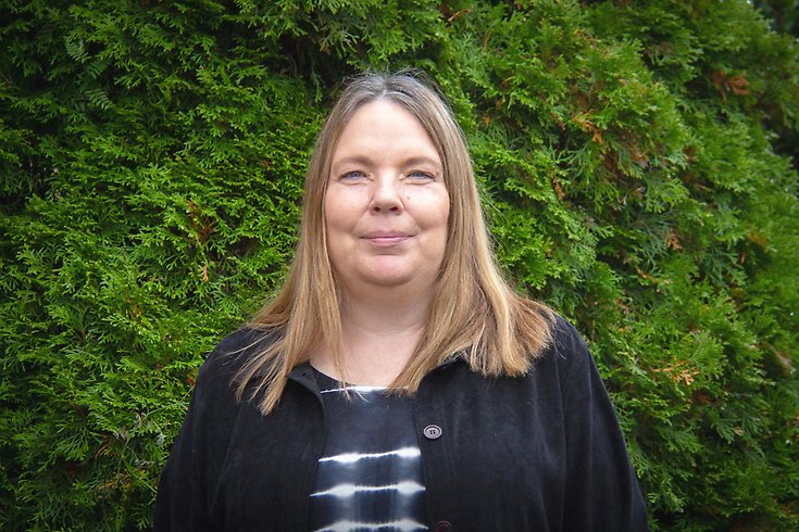 En kvinna står framför en grön buske.