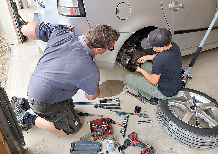 En man och en yngre kille sitter vid en bil som ska repareras.