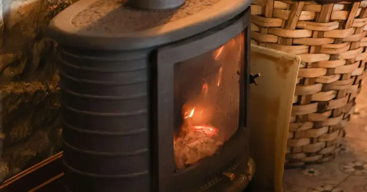 En kamin där det brinner. Intill står en korg med ved.
