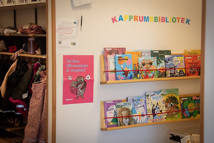 Barnböcker på hyllor i ett kapprum på en förskola.