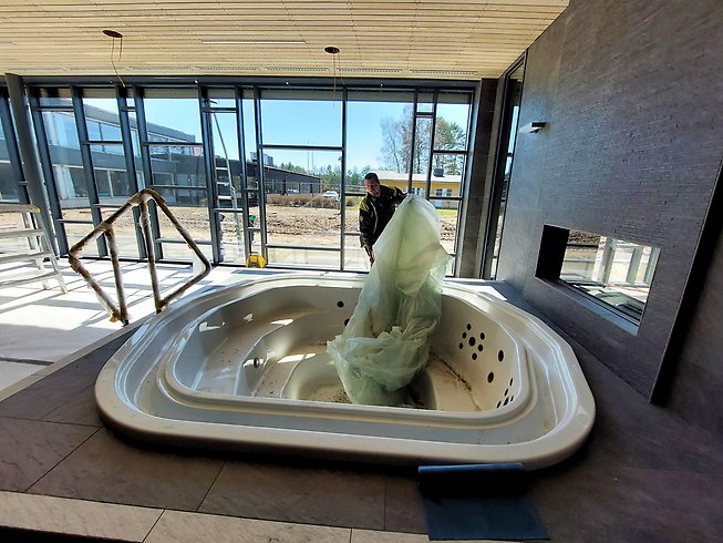 En man plockar bort plastskyddet från en bubbelpool.