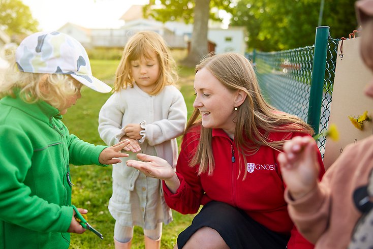 En förskolärare sitter på knä omringad av tre små barn.