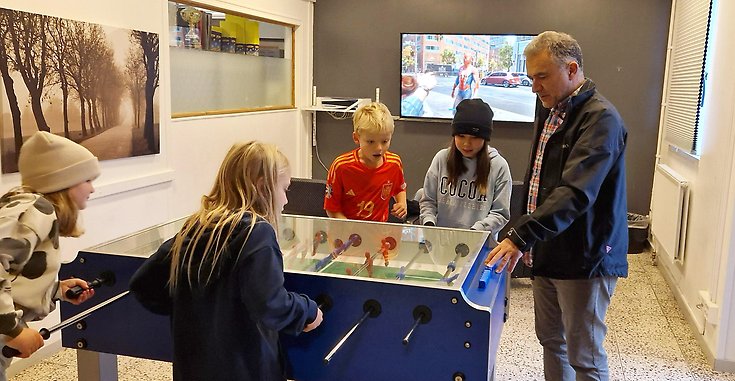 En man står vid ett bord där några barn i mellanstadieåldern spelar ett spel.