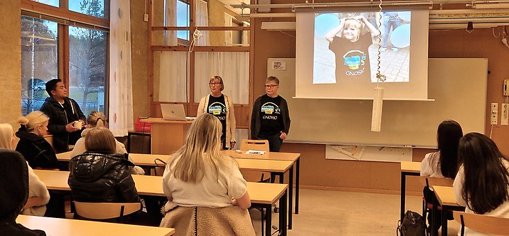 Två kvinnor står längst fram i en lektionssal.