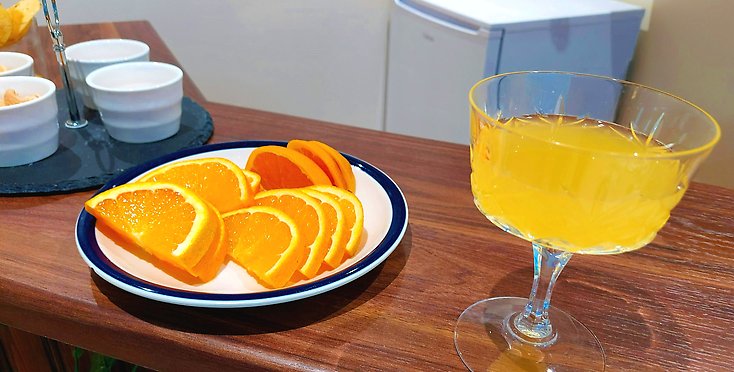 Drinkglas med gul juice och apelsiner på ett fat.