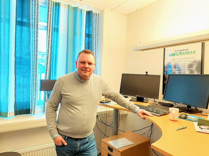 En man står mitt i ett kontorsrum framför en datorskärm.