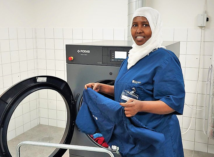 En kvinna står vid en tvättmaskin och plockar in tvätt. Kvinnan kommer från Somalia,