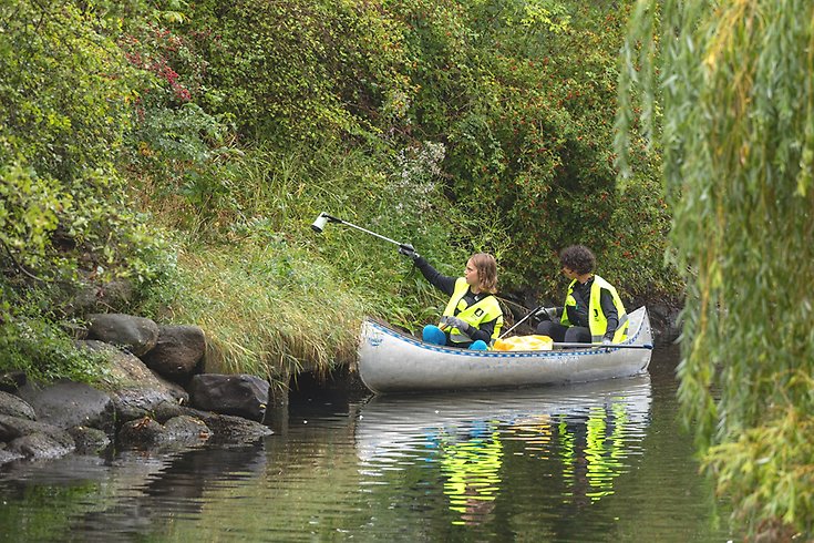 Ungdomar i en kanot plockar skräp längs kanalkanten.