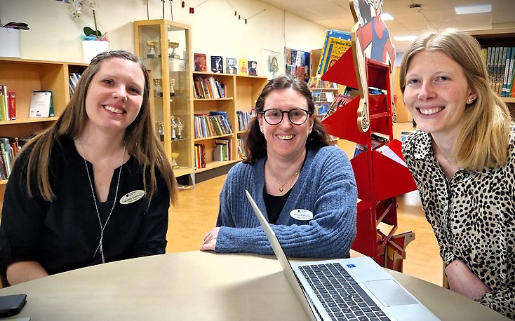 Tre kvinnor sitter vid ett bord i Åvikenskolans bibliotek.