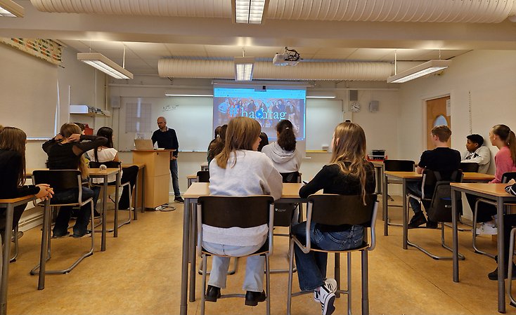 Elever sitter i sina bänkar och en lärare pratar med dem.