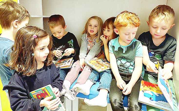 Barn sitter i en liten koja med varsin bok i sin hand.