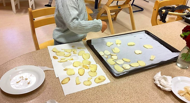 Ett barn lägger ut skivor av potatis på en plåt.