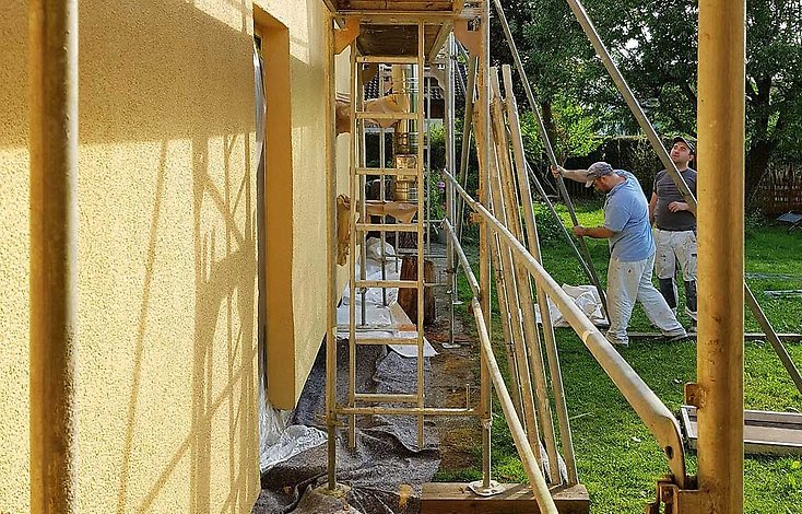 Byggställningar mot fasad, två byggjobbare.