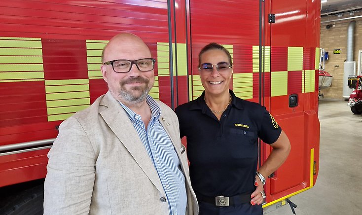 En man och en kvinna framför en brandbil, i en brandstation.