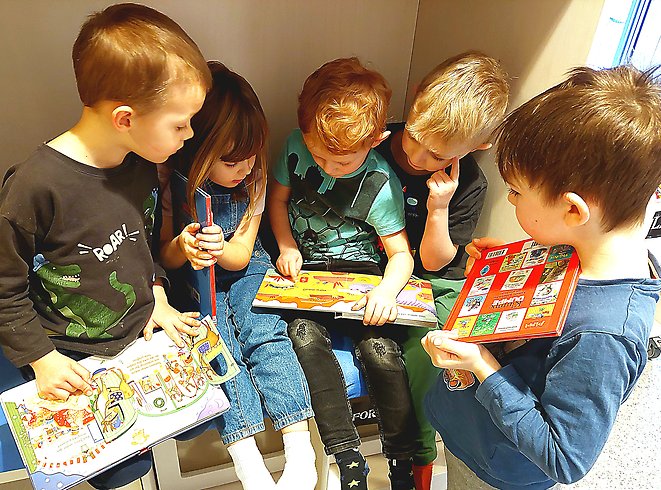 Några små pojkar sitter och läser böcker i ett krypin.