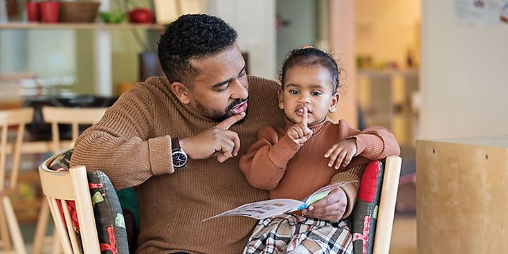 En pappa och hans dotter läser en bok tillsammans.