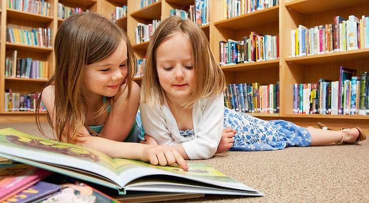 Flicor som ligger på golvet och läser böcker.