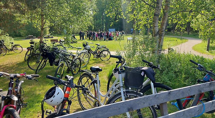 Cyklar står parkerade framför en öppen plats där barn och lärare har samlats.